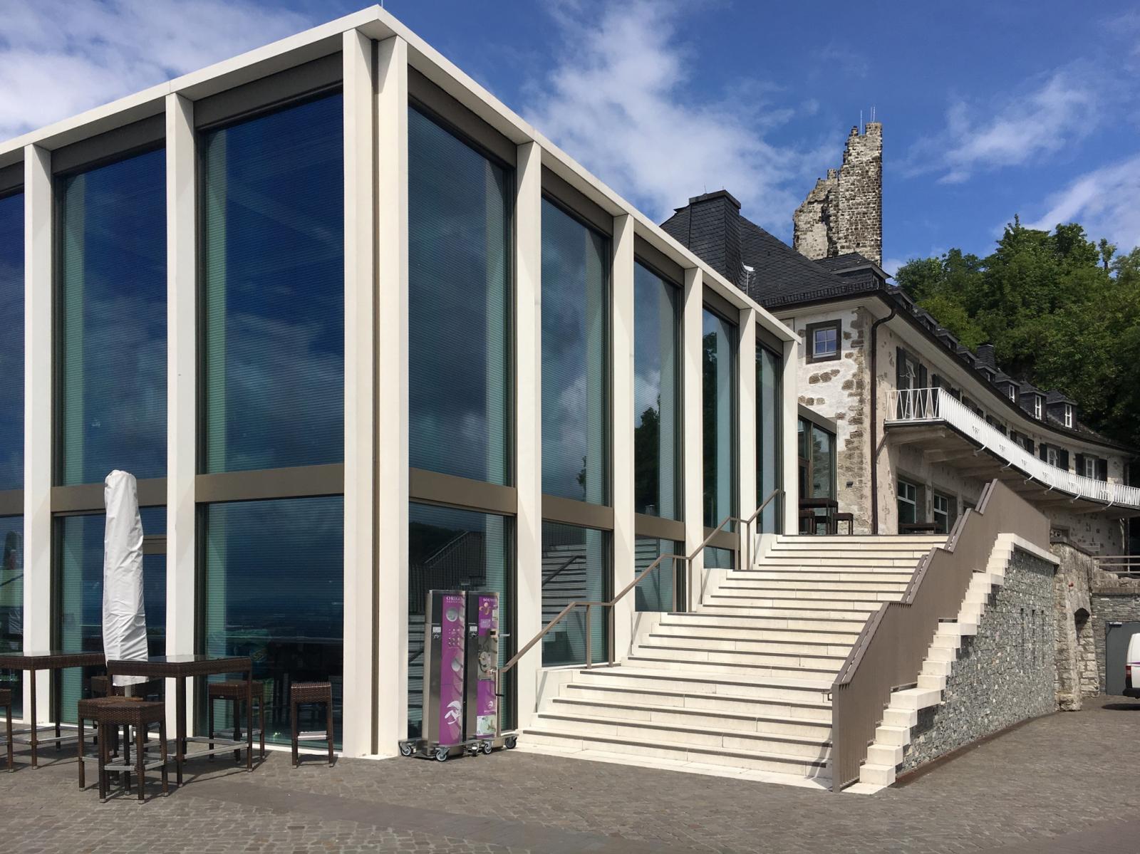 Neuer Glaskubus mit Bestandsbau und Ruine im Hintergrund