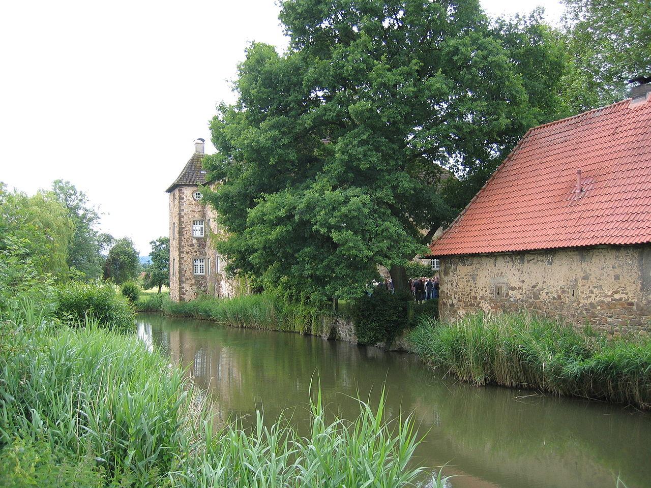 Wassergraben mit Herrenhaus im Hintergrund